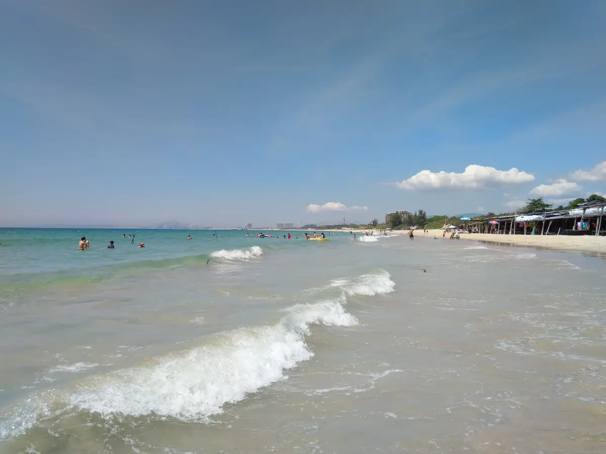 Small waves rolling onto a long sandy beach with swimmers in the distance