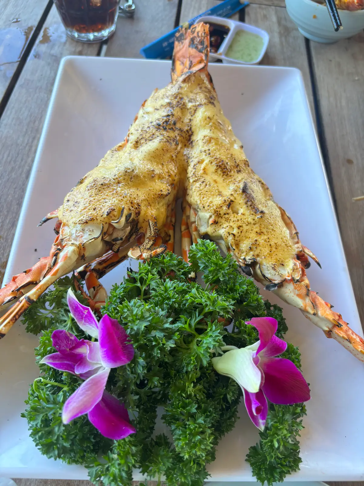 Two grilled spiny lobster halves with a golden cheese topping on a white plate with herbs