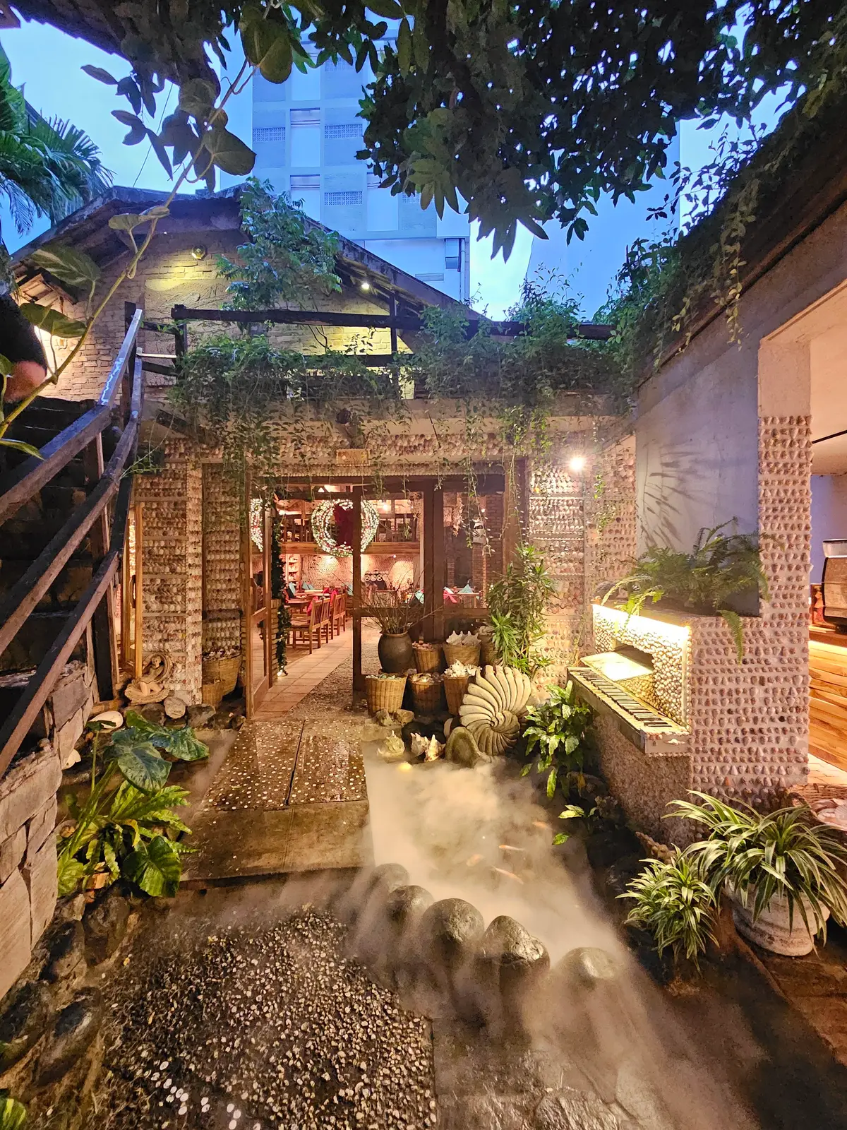 Stone and shell walled courtyard with plants, lanterns and a lit doorway