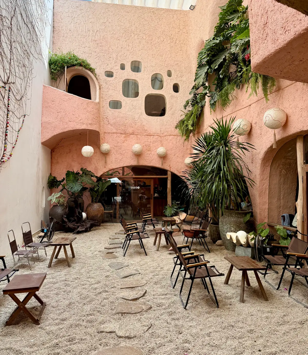 Pink clay courtyard with round lanterns, plants and wooden chairs on a gravel floor