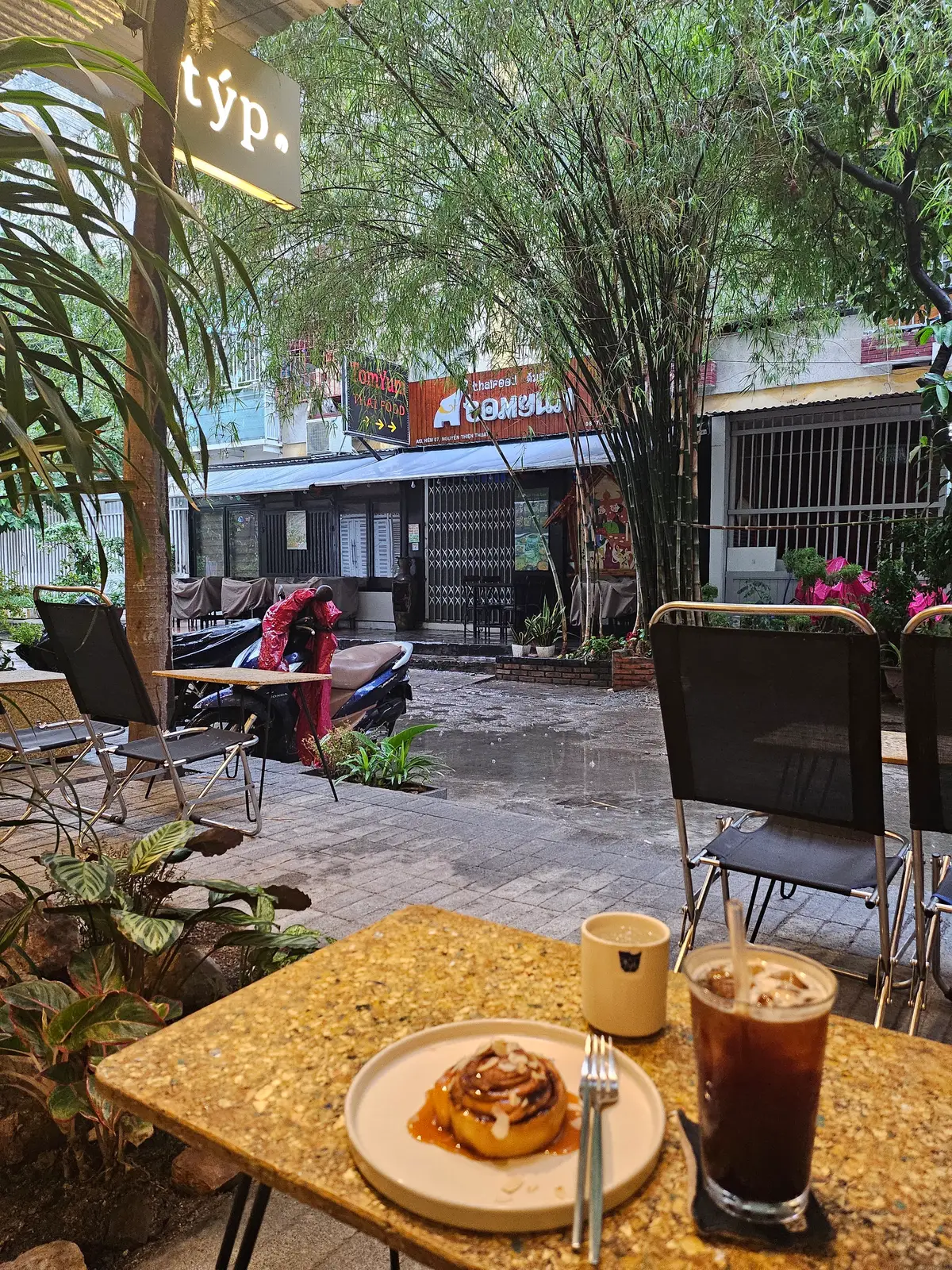Cafe terrace at dusk with dark chairs, small tables, plants and a lit Typ sign