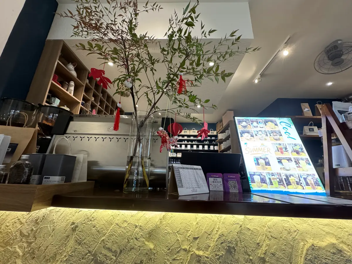 Cafe counter with a glowing yellow front, wooden shelves and a menu screen