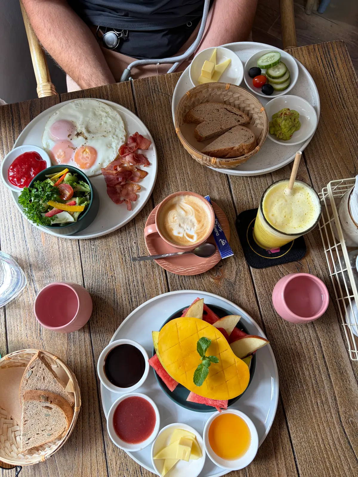 Breakfast spread with eggs, bacon, salad, fruit, a latte and a smoothie on a wooden table