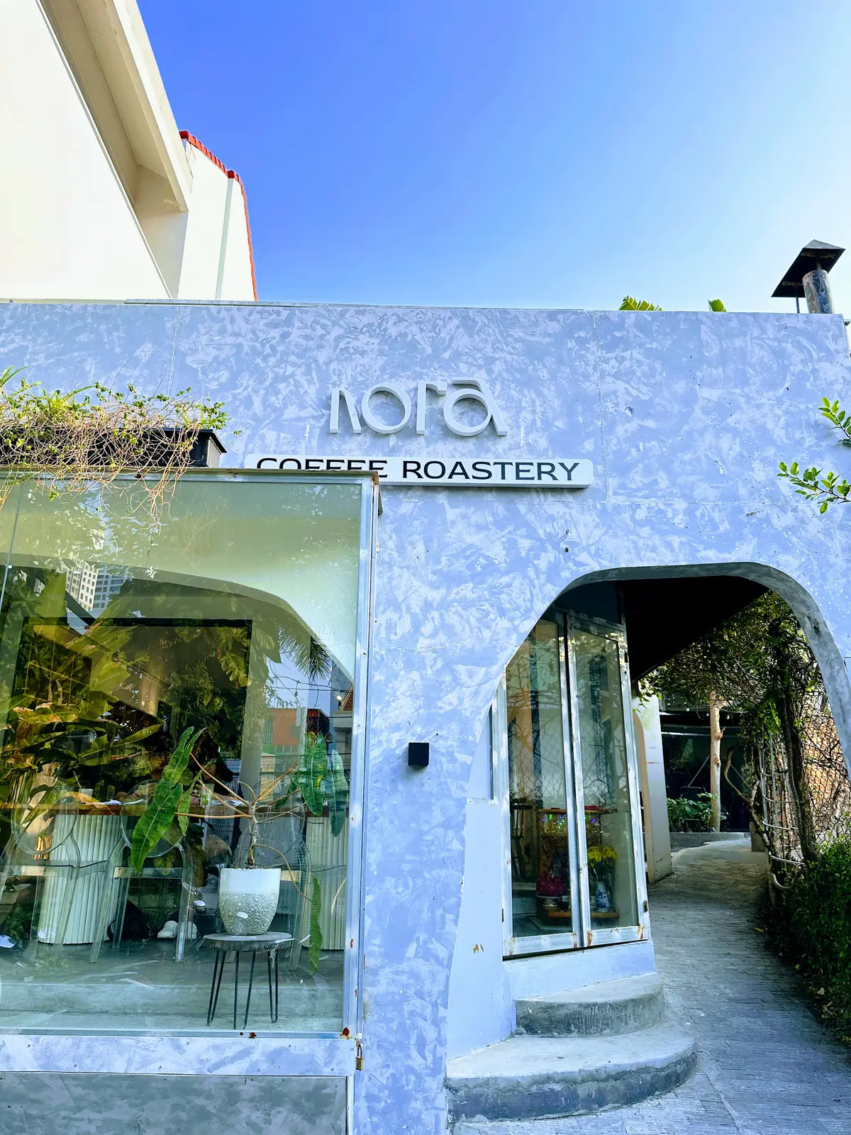 White arched cafe front with the Nora Coffee Roastery sign and plants