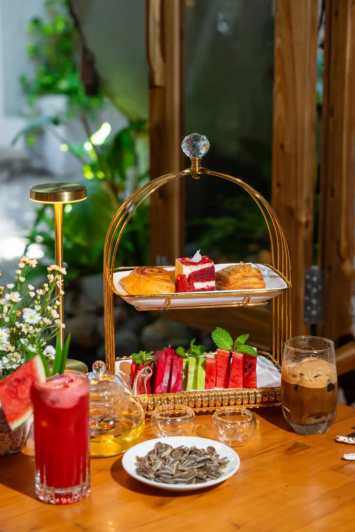 Gold tiered stand with cakes and watermelon slices beside a cold coffee