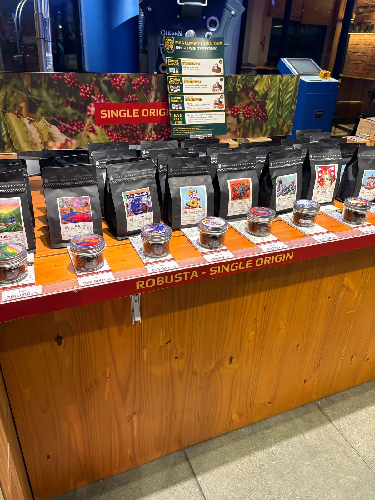 Display shelf of coffee bean bags with small sample jars under a Robusta sign
