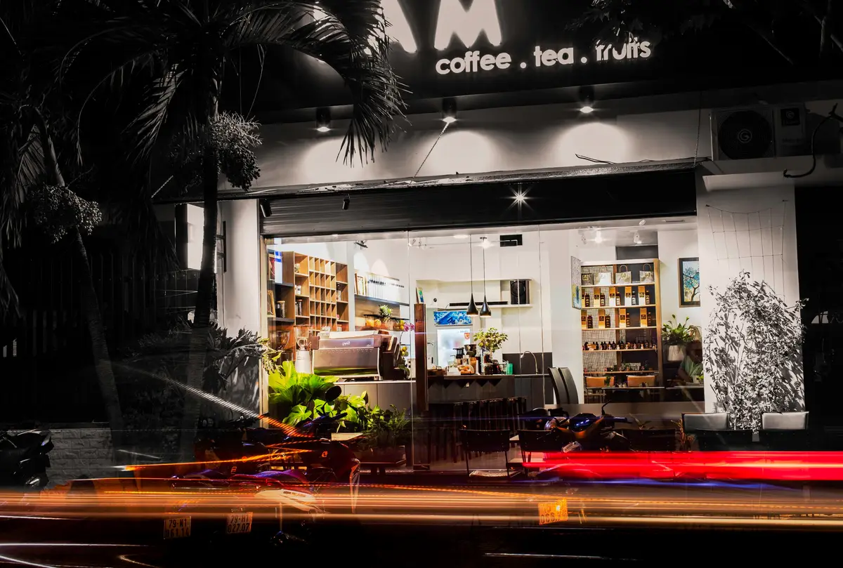Evening street view of a glass-fronted cafe with wooden shelves inside