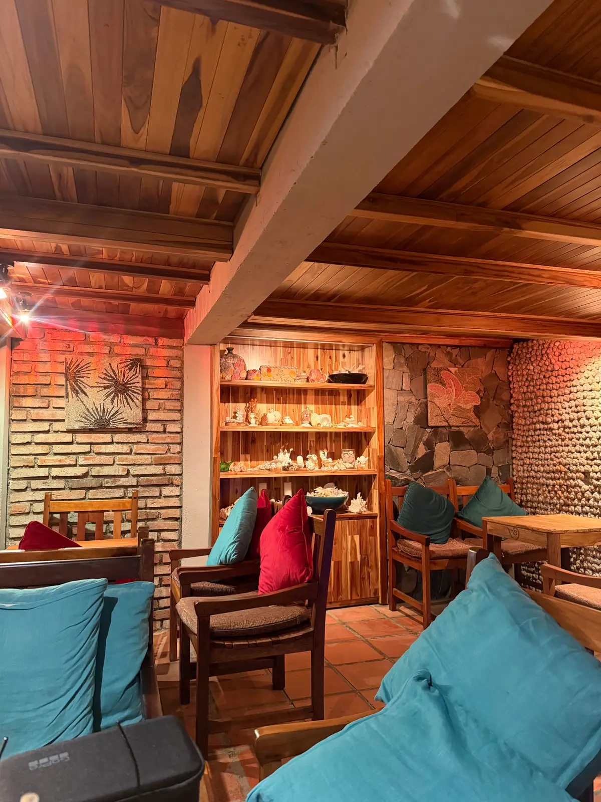 Wooden cafe corner with brick wall, shelves of shells and red and teal cushions