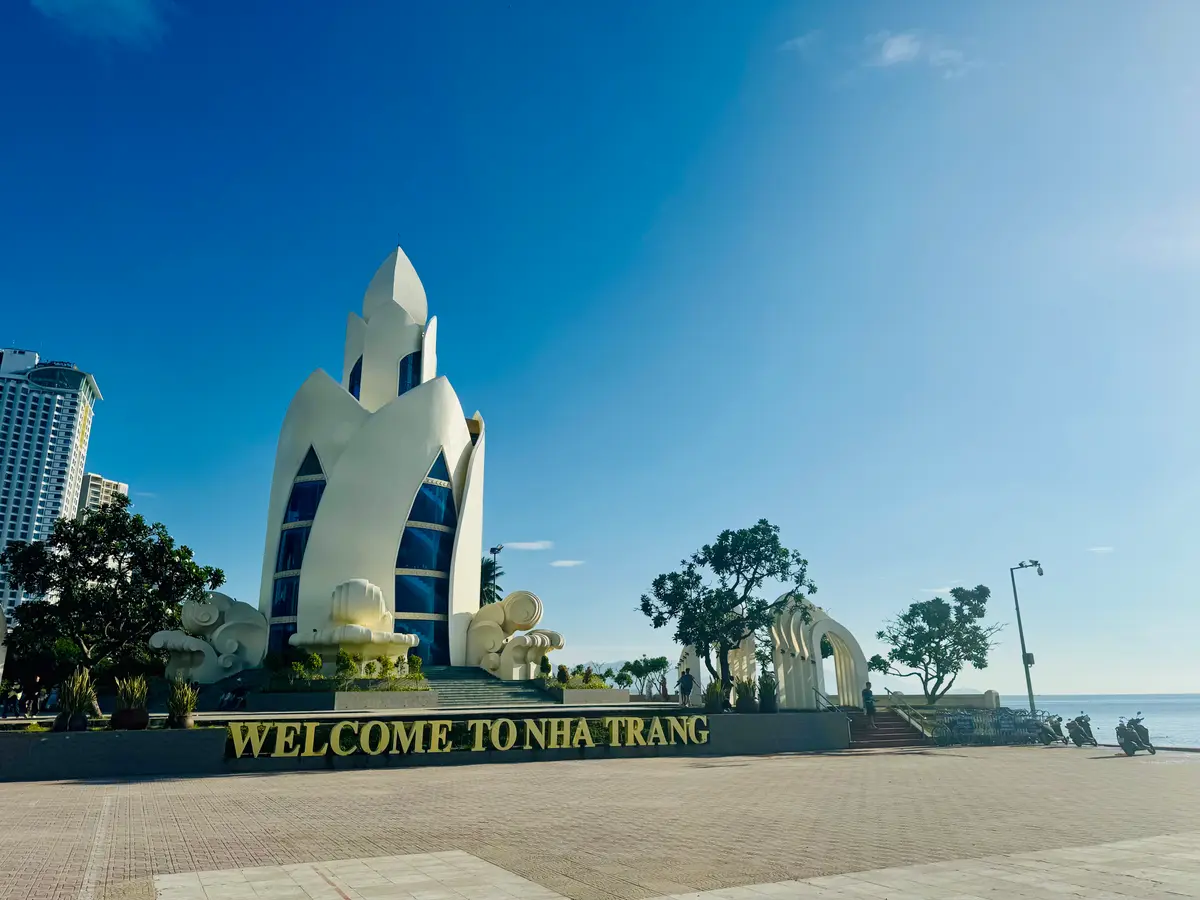 White lotus-shaped tower on the Nha Trang seafront under a bright blue sky, with a welcome sign in the foreground