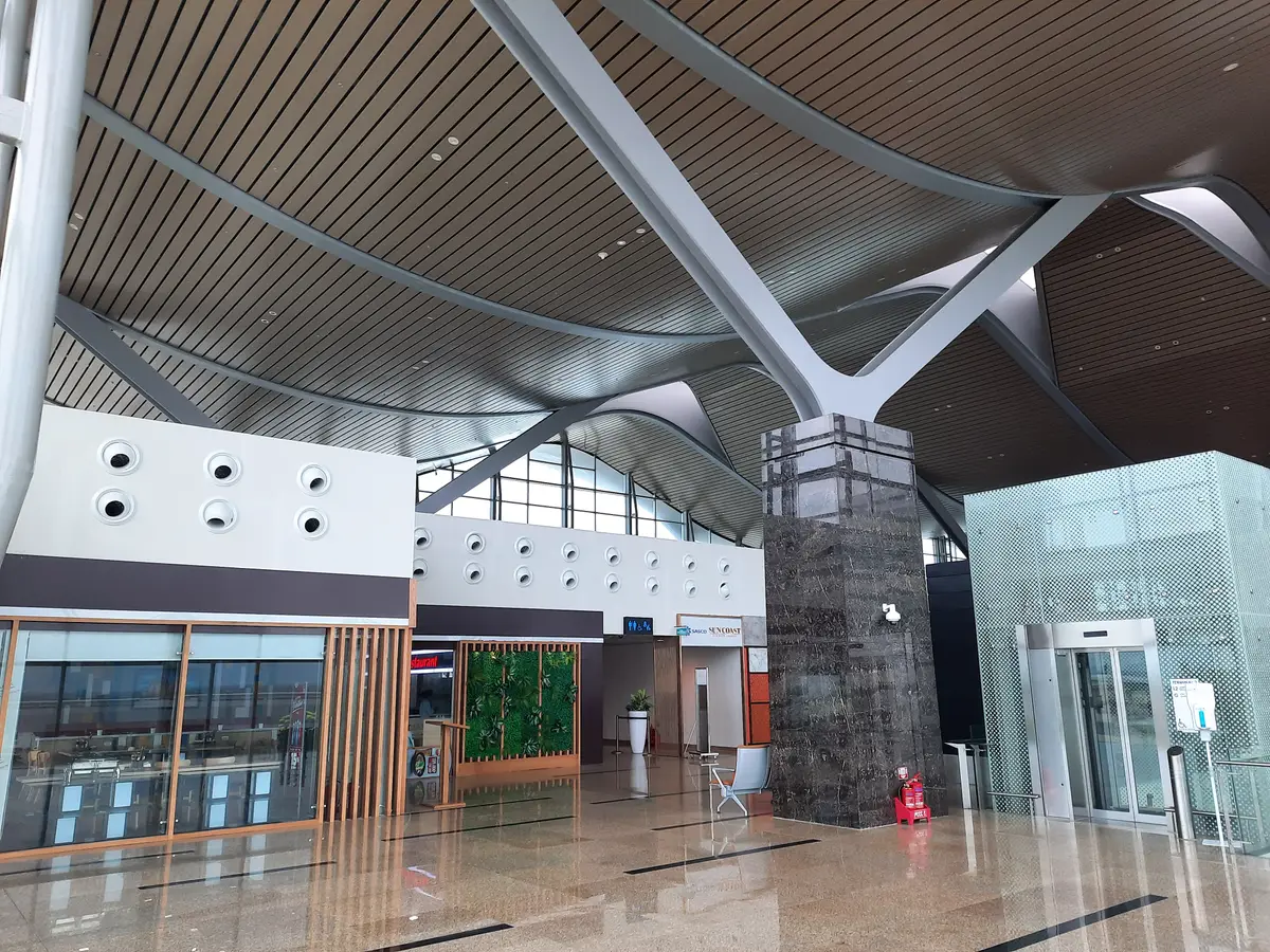 Empty terminal hall with tall white support columns, a glass wall and a shiny floor.