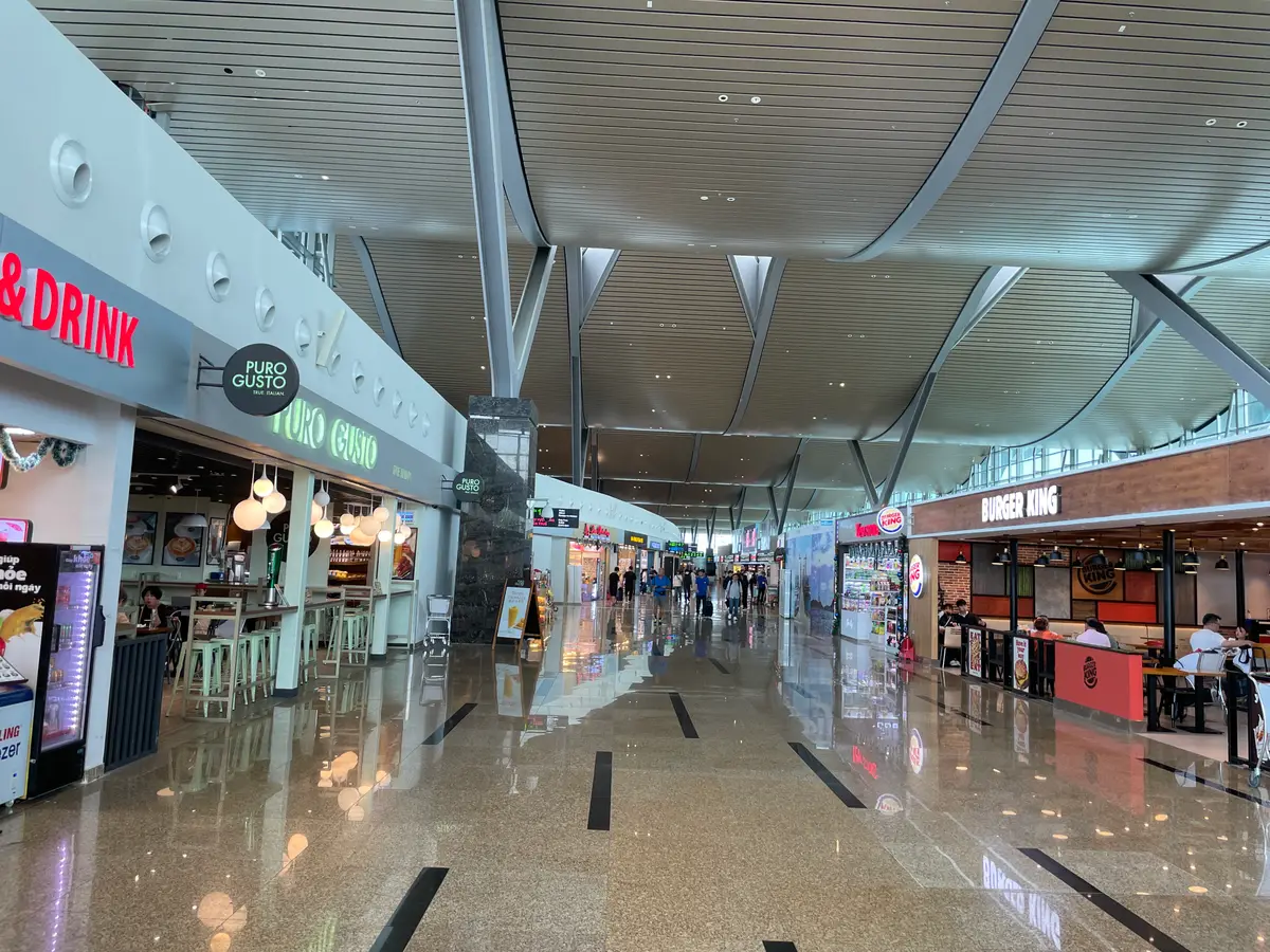 Long airport concourse with shops on both sides and a high roof structure.
