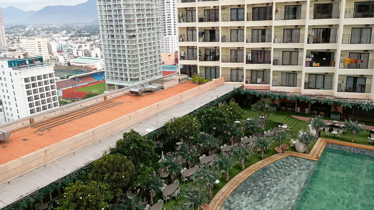 View from a high floor over a landscaped rooftop garden and swimming pool beside an apartment block