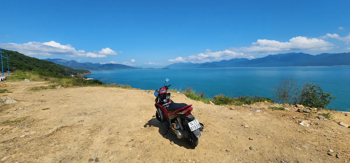 Red scooter parked on a dirt viewpoint above a blue bay