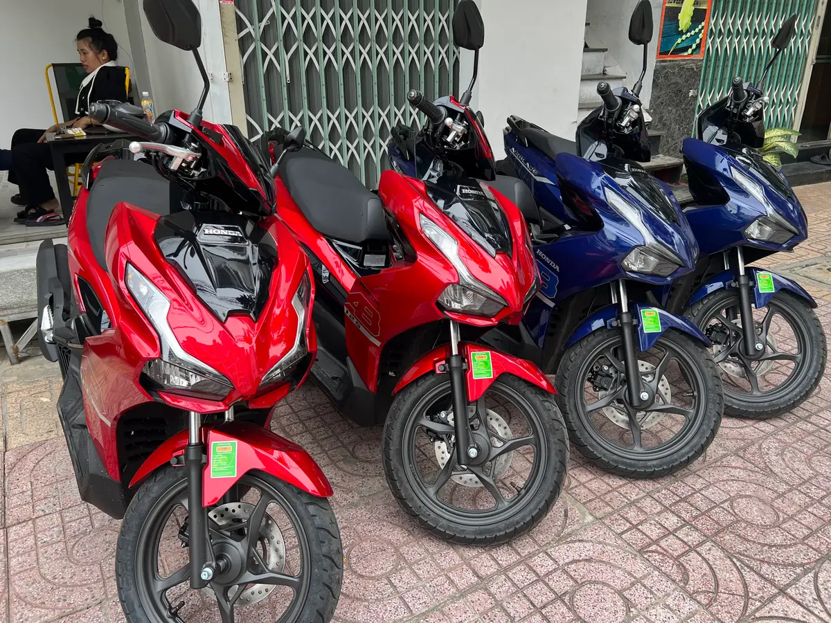 Row of red and blue scooters parked outside a rental shop on a tiled pavement