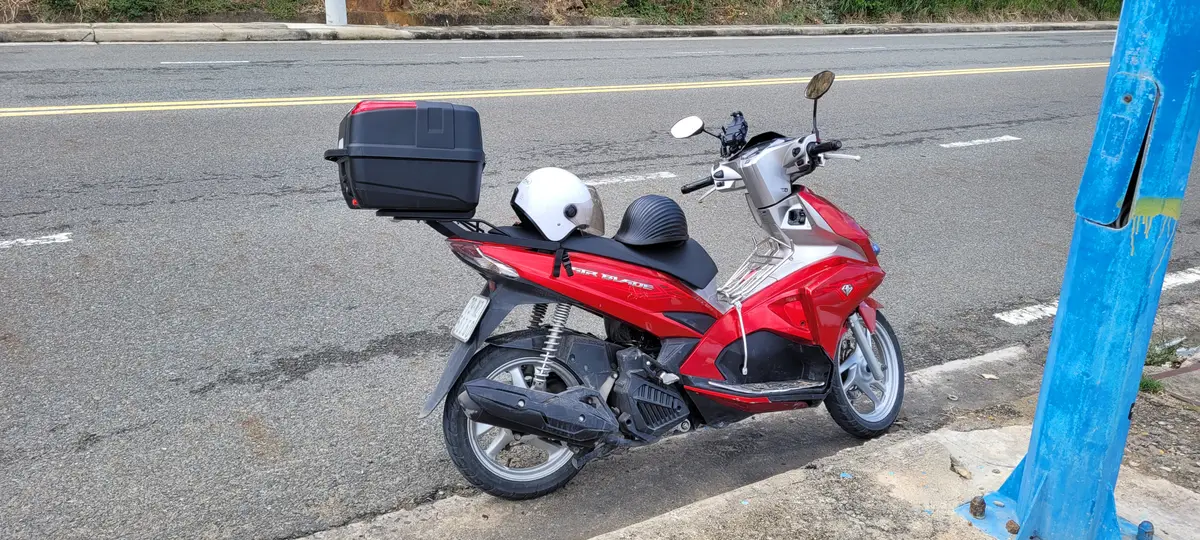 Red scooter with a helmet on the seat and a luggage box parked at the roadside