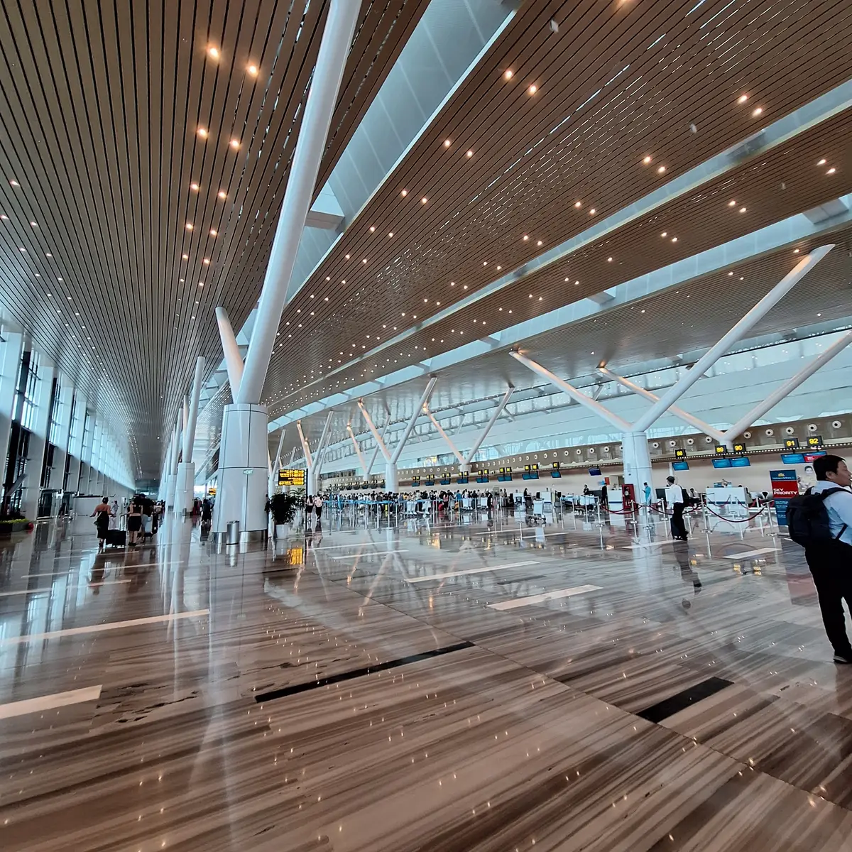 Long terminal hall at Cam Ranh airport with a wood-slat ceiling, white support columns and a polished floor with a few travellers walking.