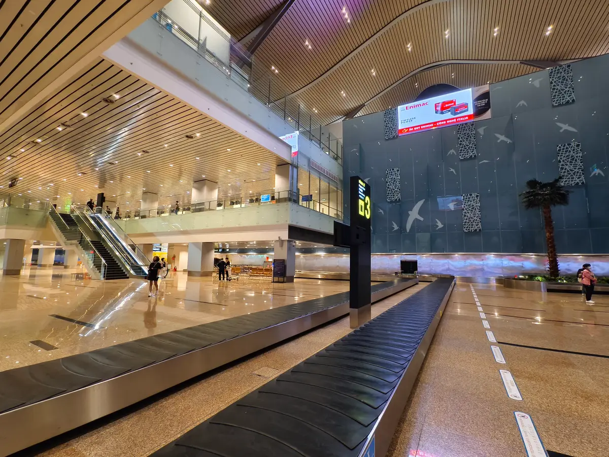 Baggage claim hall at Cam Ranh Airport with a carousel and an escalator.