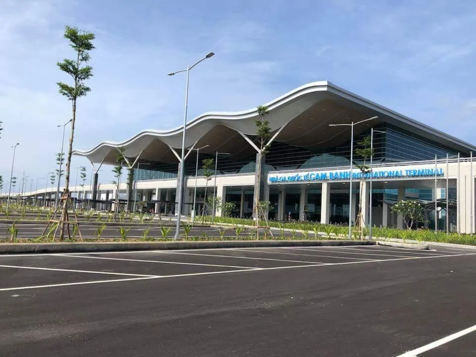 Cam Ranh International Airport passenger terminal with a wave-shaped roof, a car park in front and the airport name on the facade