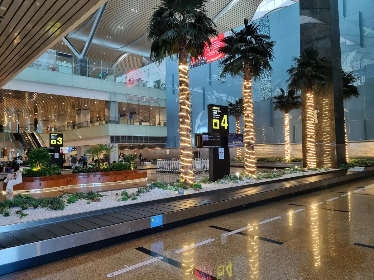 Arrivals hall at Cam Ranh International Airport with palm trees, a baggage belt and a gate number sign