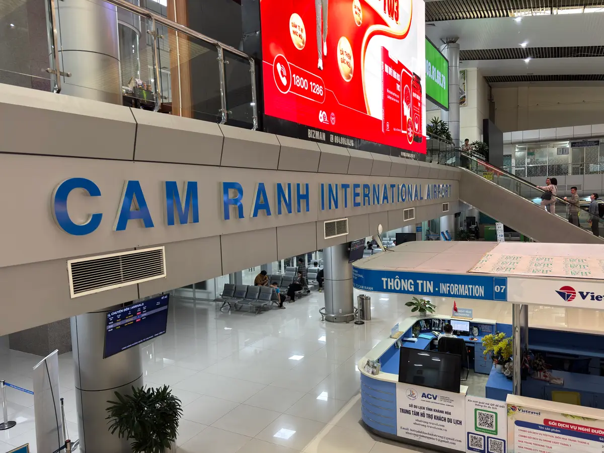 Terminal hall at Cam Ranh International Airport with a large blue airport sign, an information desk and an escalator