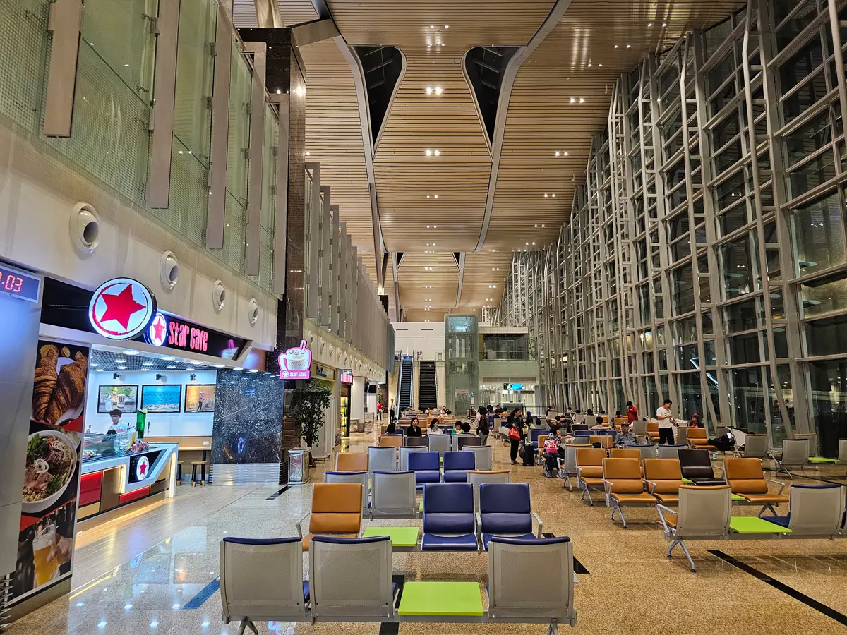 Departure hall at Cam Ranh International Airport with rows of seats, food outlets on the left and a tall glass facade