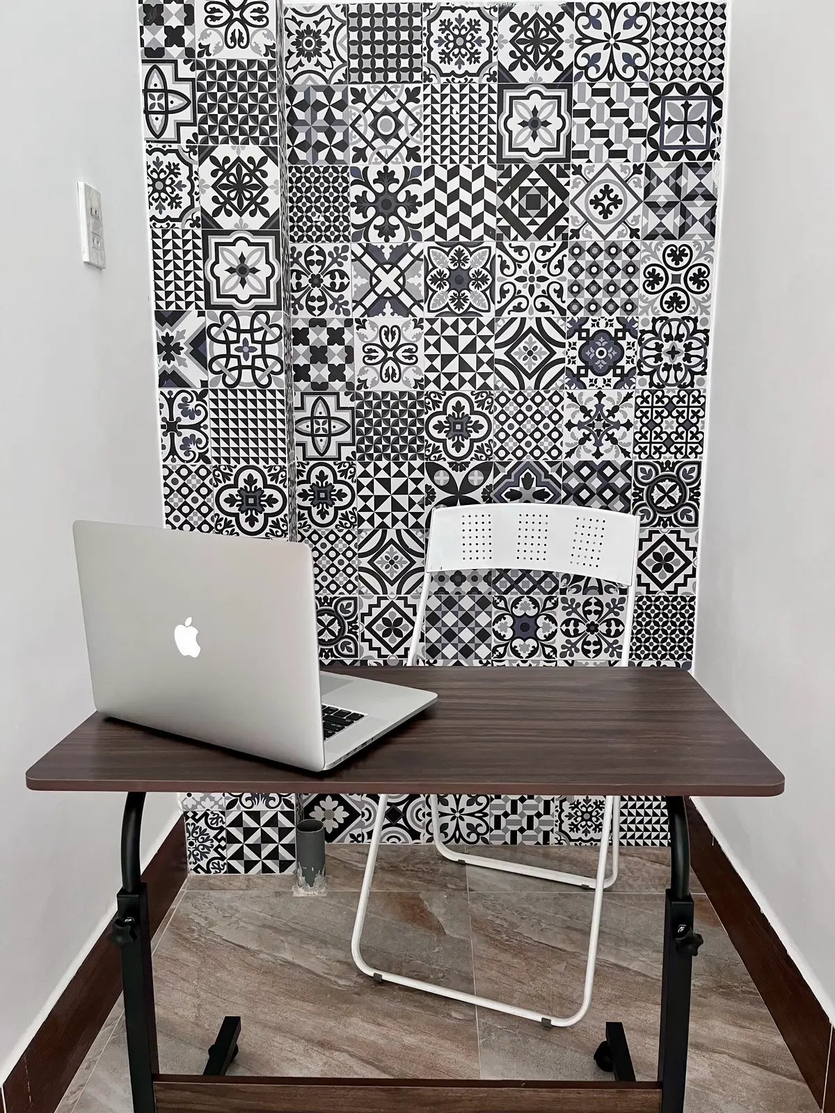 Laptop on a dark wooden desk with a white chair in front of a black and white patterned tile wall