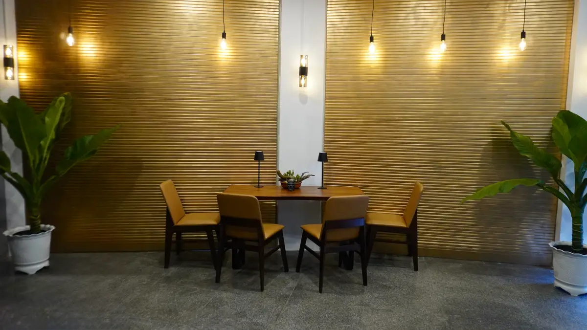 Wooden dining table with four chairs against a wall of wood slats and pendant lights