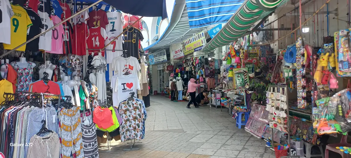 Covered market alley with hanging T-shirts and souvenir stalls on both sides