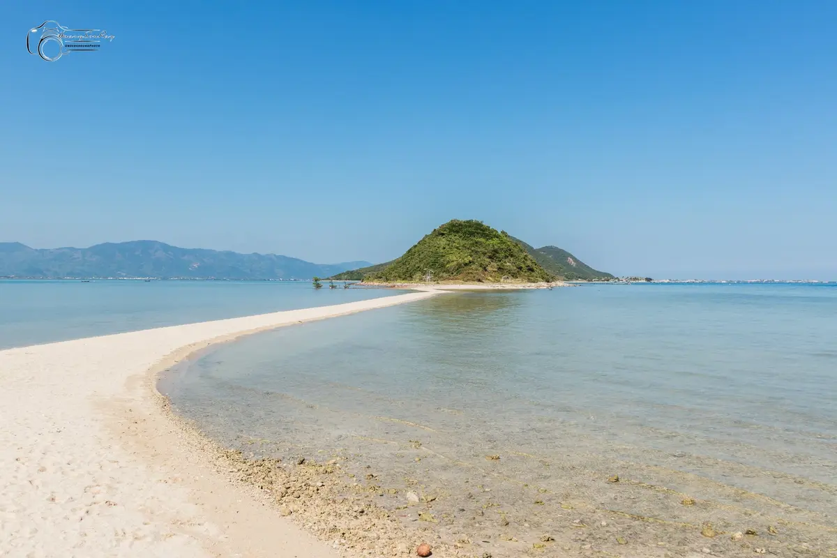 Narrow white sandbar curving into the sea toward a green island