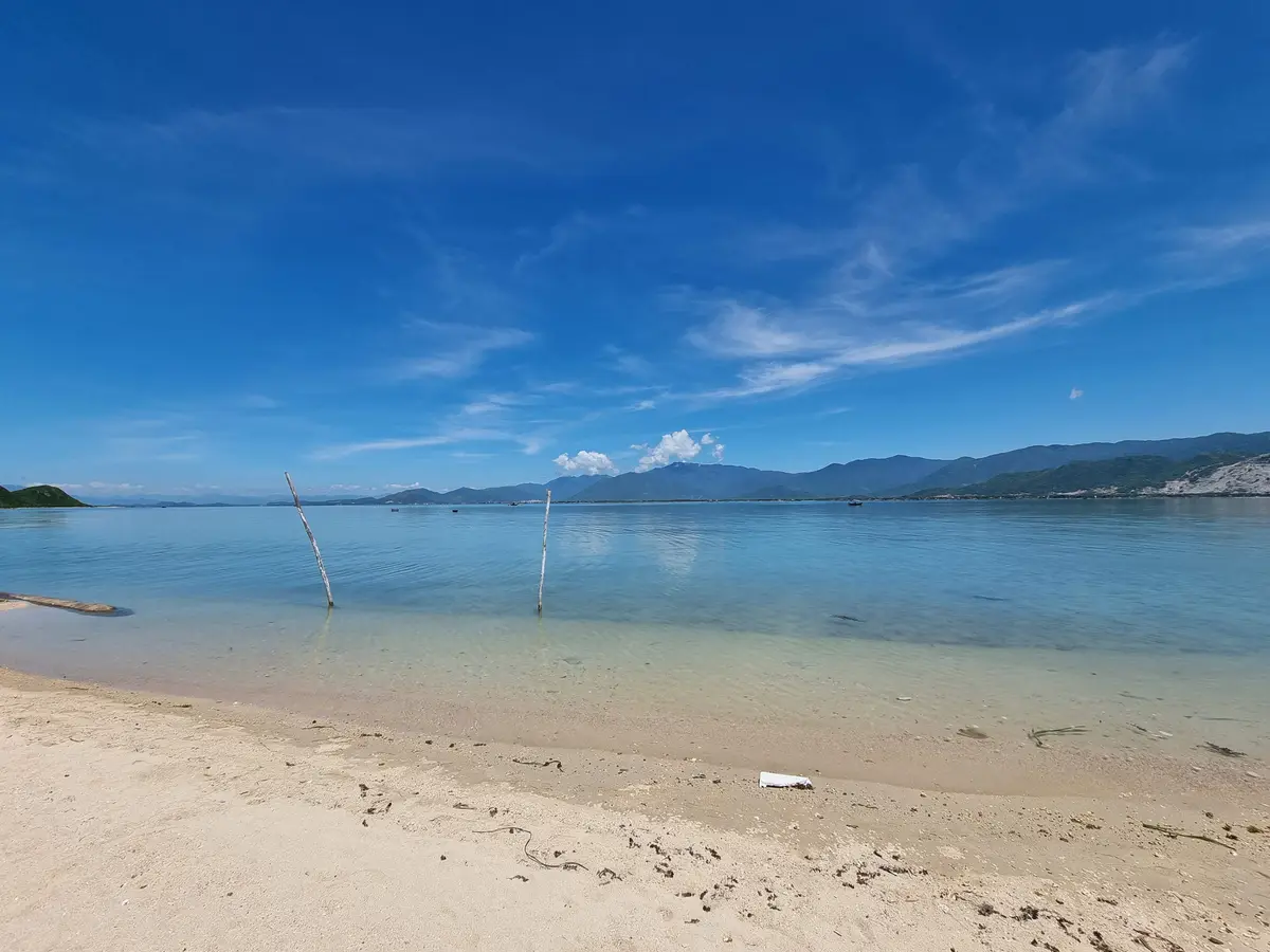 Pale sand beach and shallow clear water under a blue sky with hills far off