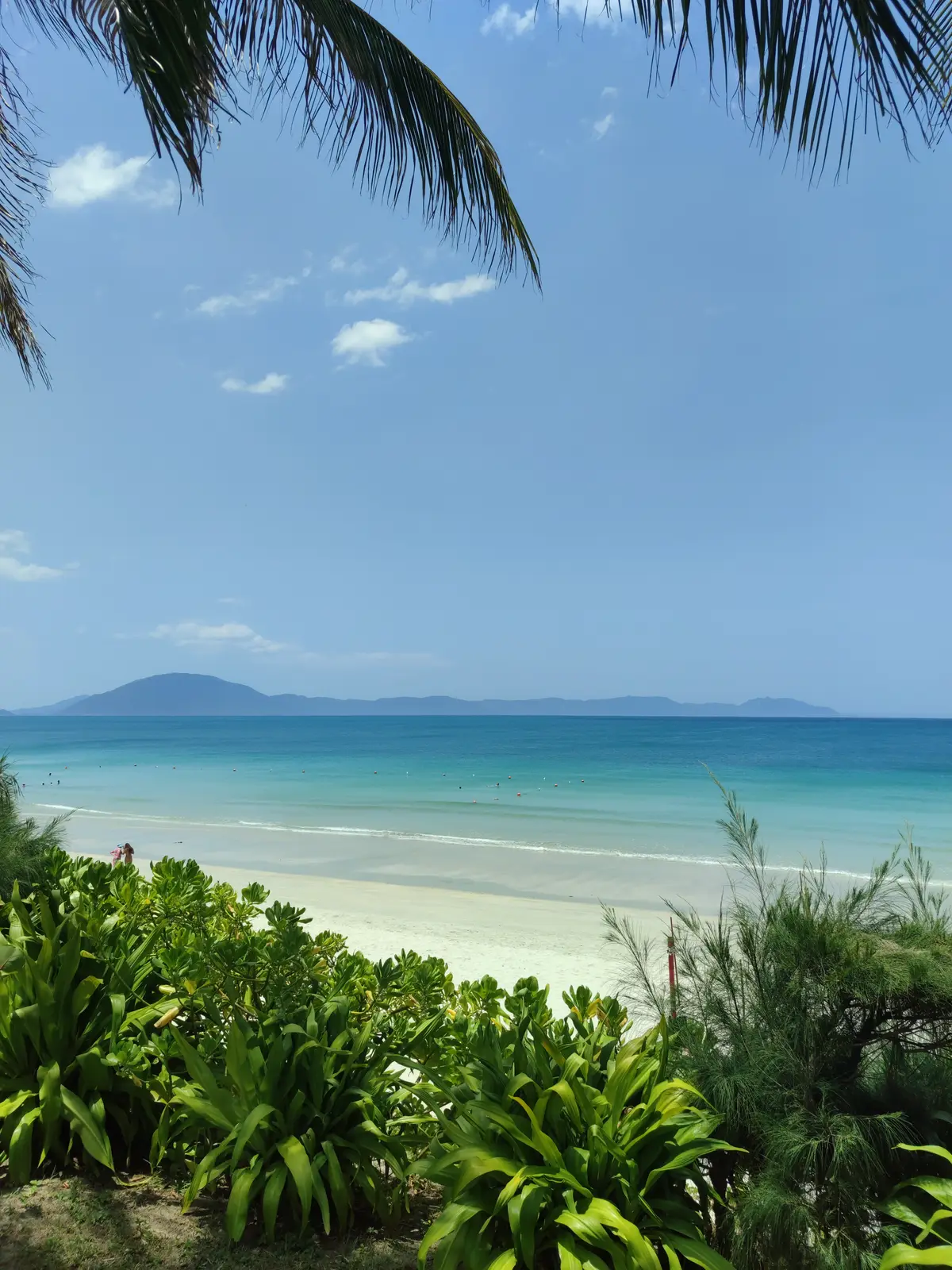 Pale sand beach and turquoise sea with a low island on the horizon