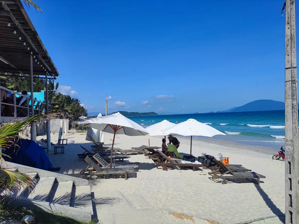 Parasols and wooden sunbeds on the sand with mountains across the bay