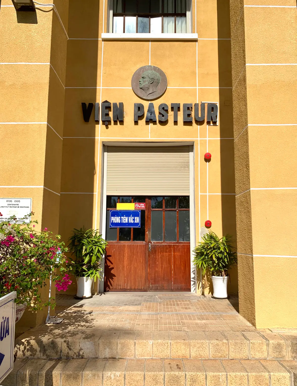 Yellow building entrance with the institute name above a closed shutter and a vaccination room door