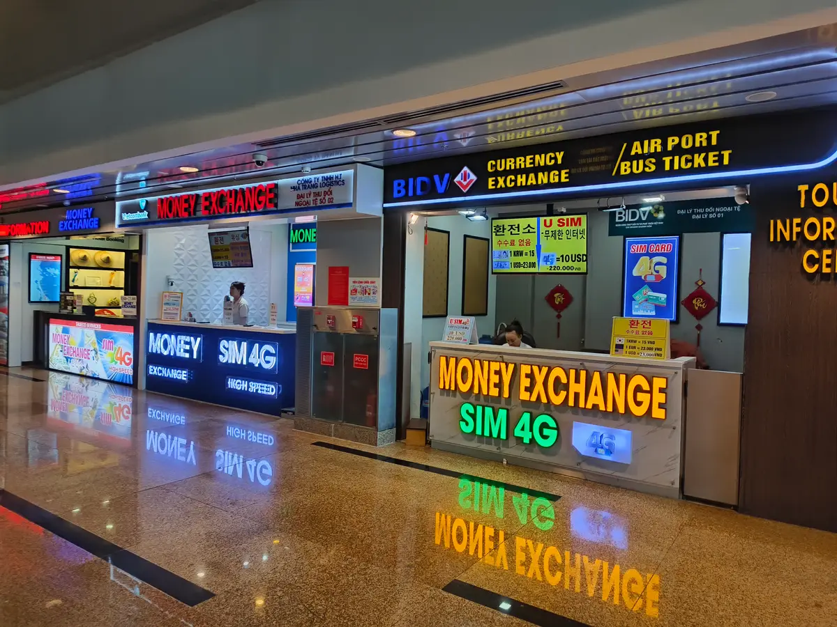Currency exchange and SIM 4G counters with lit signs inside the arrivals hall at Cam Ranh International Airport