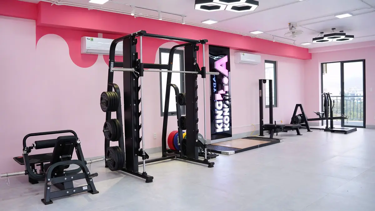 Black weight rack with a barbell against a pink wall in a gym