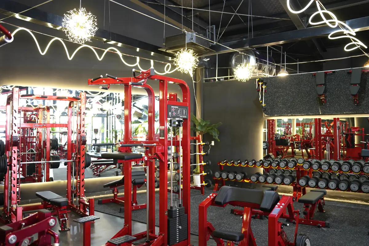 Red weight racks and benches on the Tho Gym floor under string lights