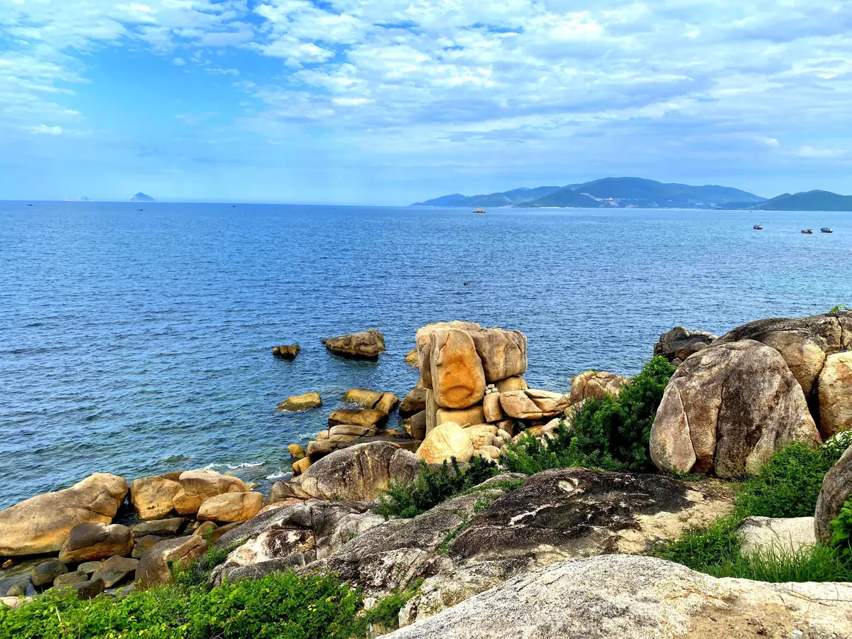 Golden boulders on a rocky shore above blue sea with a distant island