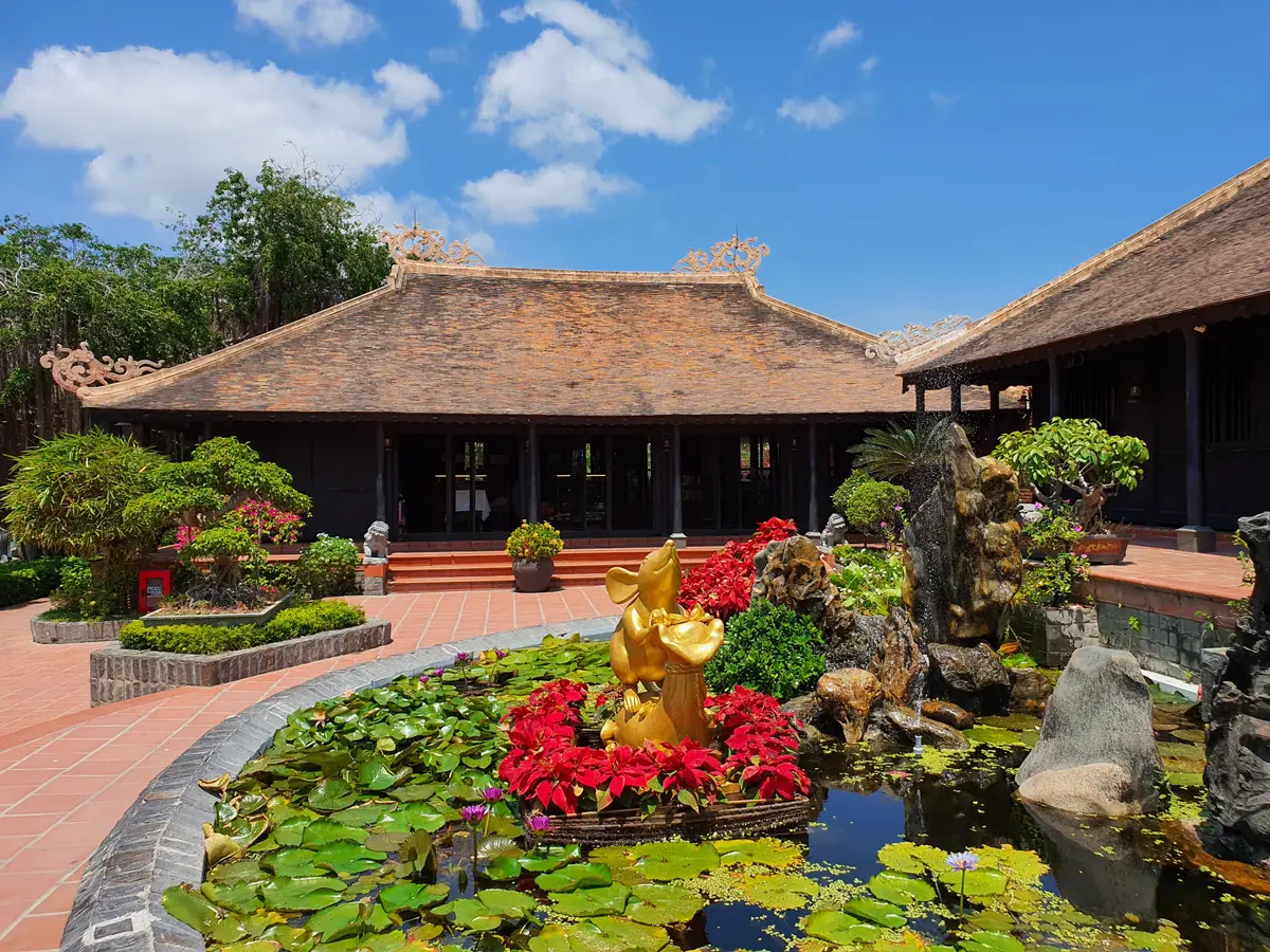 Thatched pavilion beside a lotus pond with red flowers and a golden statue
