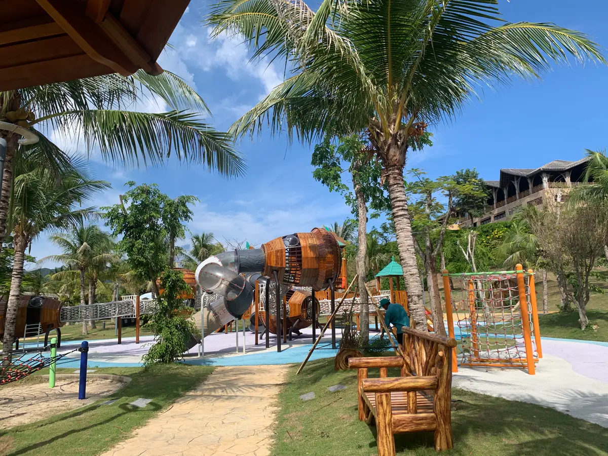 Children's playground with wooden climbing frames under palm trees