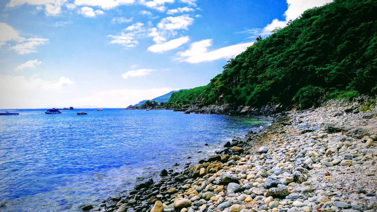 Pebble shore beside deep blue water below a green headland