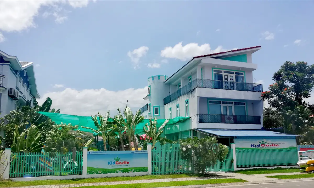 A white and blue three-storey building behind a green fence under a blue sky.