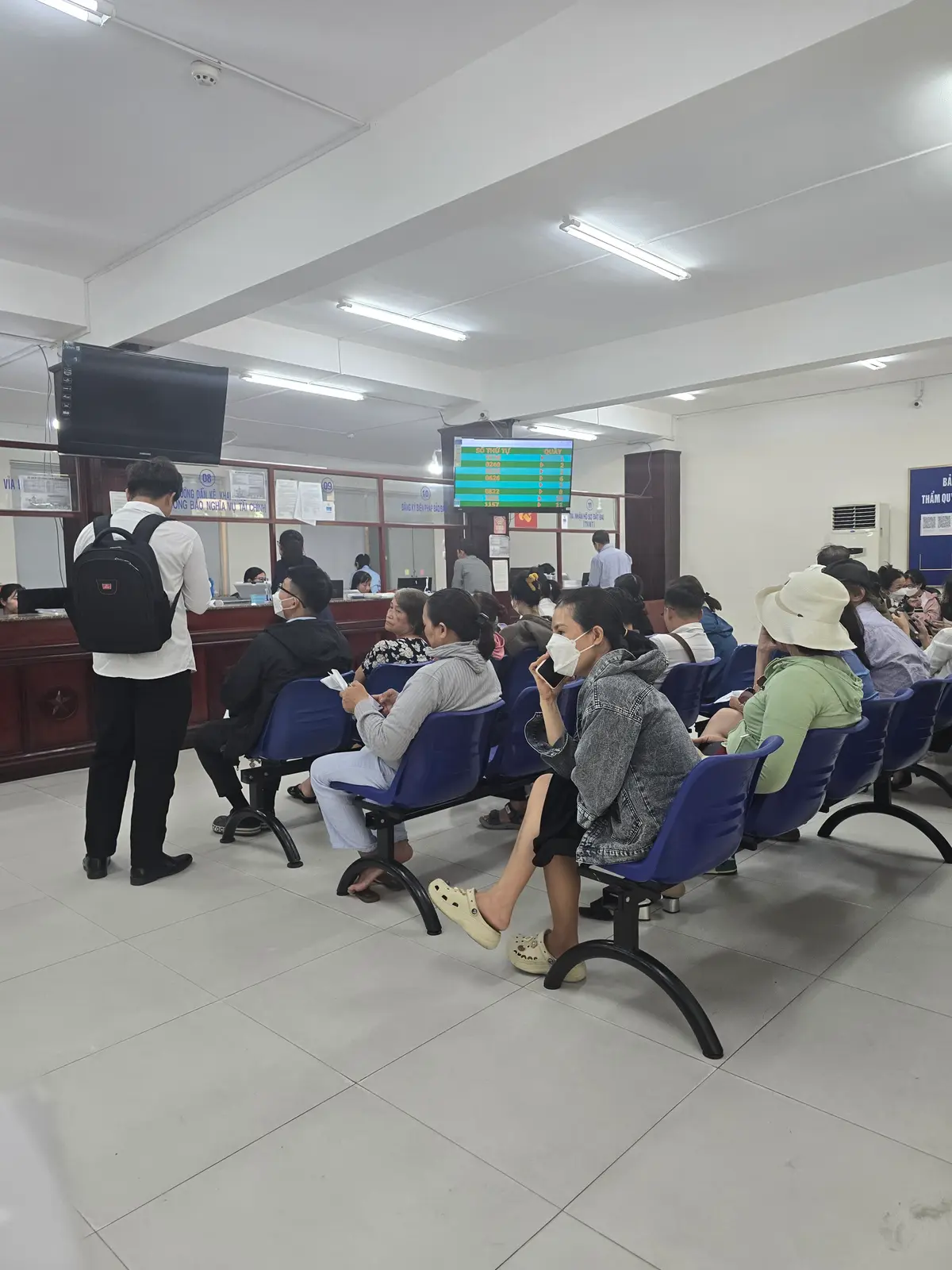 Waiting area of a public service counter with rows of blue seats and people waiting to be called.