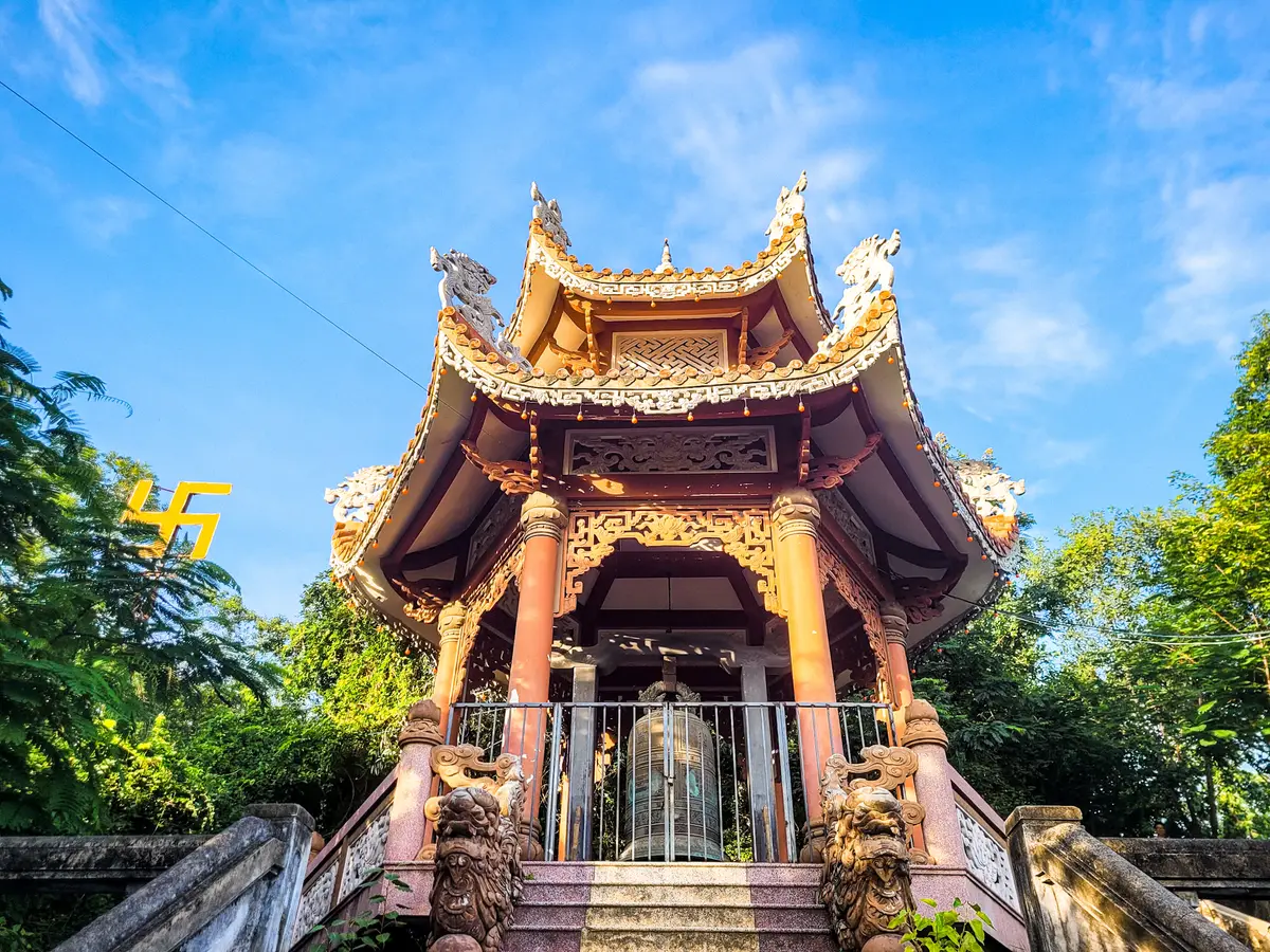 Carved wooden bell pavilion with a curved gold roof among trees