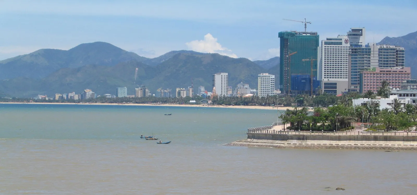 Nha Trang bay with high-rise buildings along the shore, mountains behind and a few boats on the water.