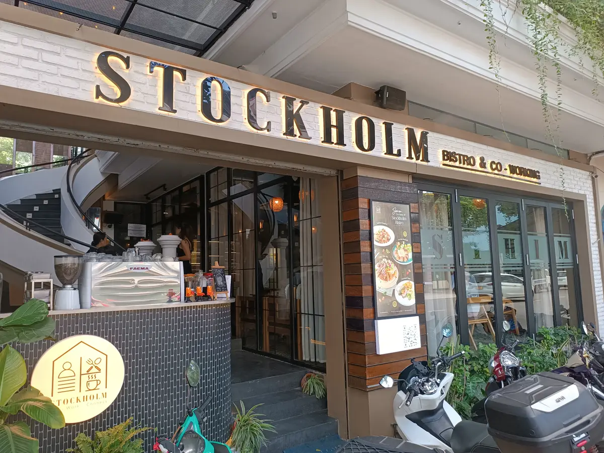 Street front of a restaurant and co-working building with a gold Stockholm sign above glass doors and a coffee counter inside