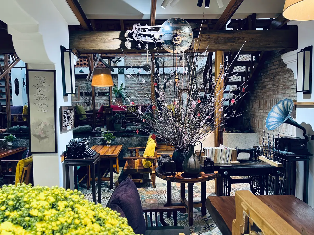 Interior with dark wooden beams, a staircase, vintage furniture, framed pictures and a gramophone beside yellow flowers