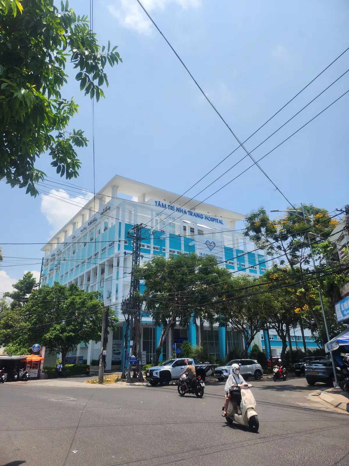 White and blue hospital building with trees and street cables in front