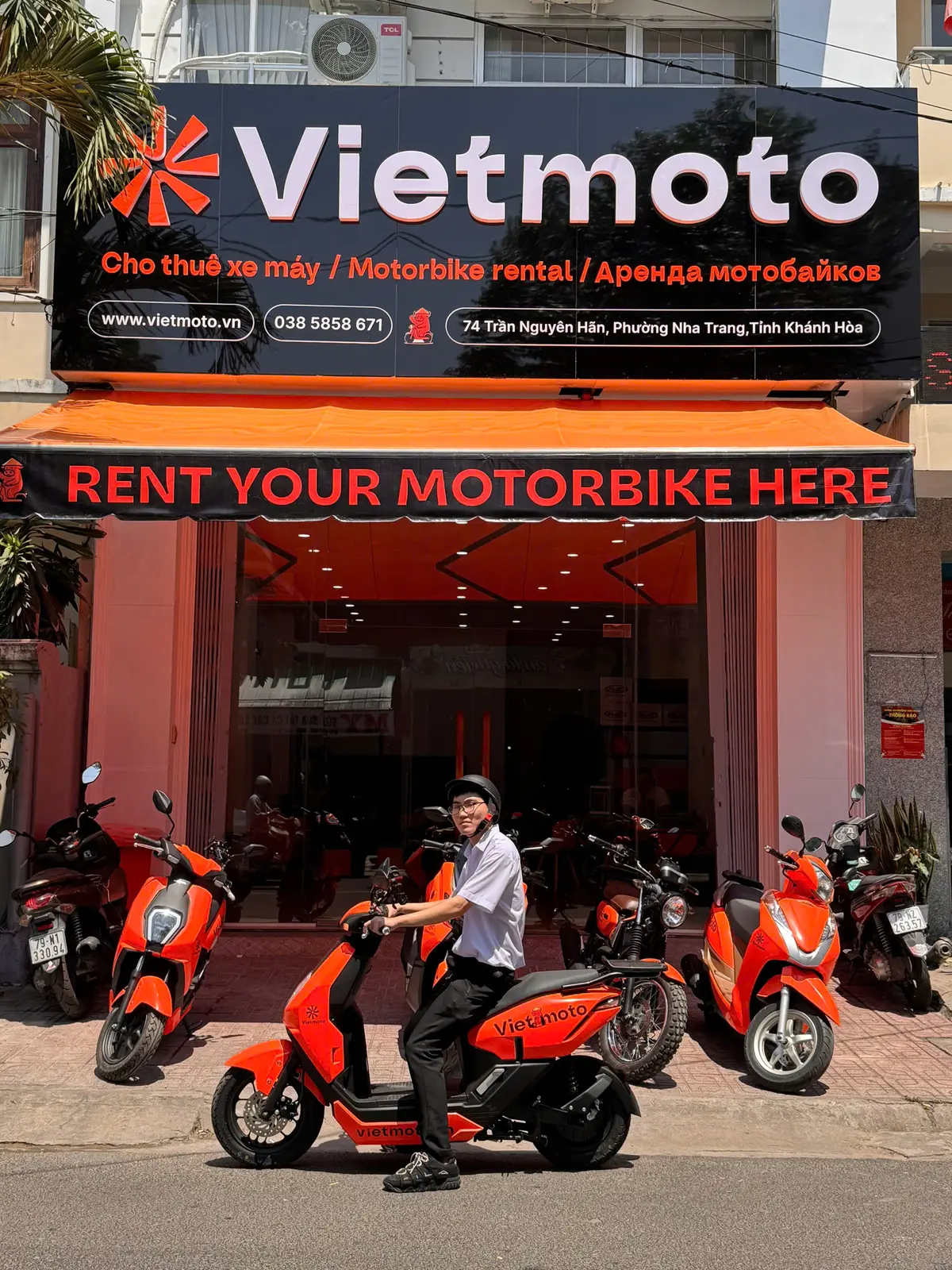 Shopfront with a red banner reading Rent your motorbike here and orange scooters parked in front