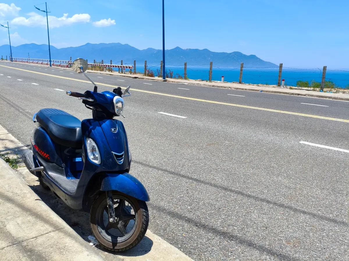 Blue scooter parked at the roadside beside a sea view and mountains