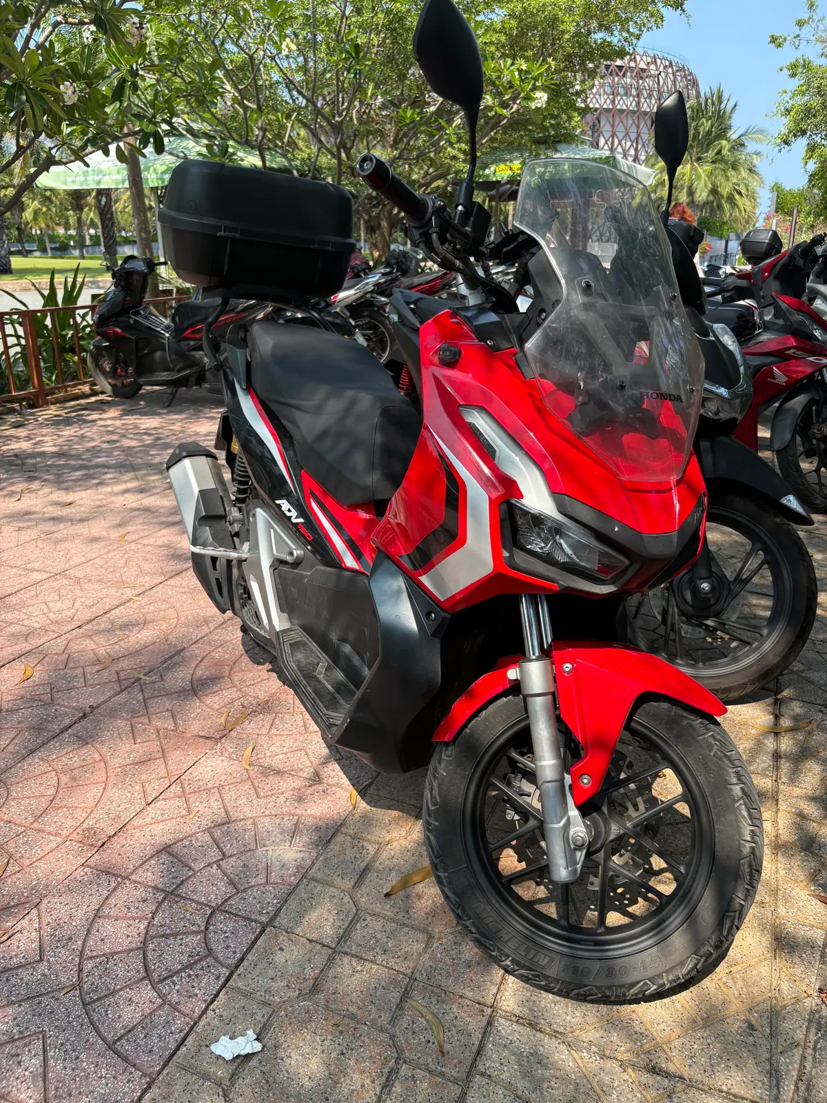 Front of a red adventure scooter with a tall windscreen parked among other bikes